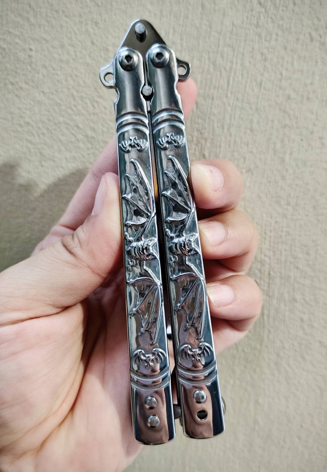 🦇 มีดควงค้างคาว เป็นบาลิซองสแตนเลส ขัดเงาเต็มตัว ใบทรงทันโตะ ปลายเฉียบ เส้นคมคมชัด ดูมีพลัง ด้ามแกะลายค้างคาวกางปีก รายละเอียดสวย งานนูนคมจนสัมผัสได้ ทั้งใบและด้ามเป็นสแตนเลส แข็งแรง จับแล้วรู้สึกถึงน้ำหนักพอดีมือ สายสะสม / สายชอบงานเงา / สายเท่เร