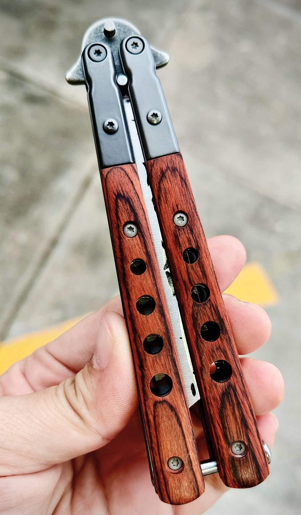 มีดควงบาลิซอง ทรงใบคัตติ้งปลายเฉียบ ไล่ลวดลายผิวใบแบบตีผิวดิบ ดูมีเอกลักษณ์ ด้ามผสมสแตนเลส + ไม้ ให้ฟีลแข็งแรงแต่ยังจับสบายมือ ตัวด้ามจับแน่น ไม่คลอนง่าย มีน๊อตยึดอย่างดี เวลาหมุนแล้วคุมจังหวะได้ดี น้ำหนักสมดุล ขนาดพอดีมือ ใช้โชว์ก็เท่ห์ ใช้งานก็ลงตัว