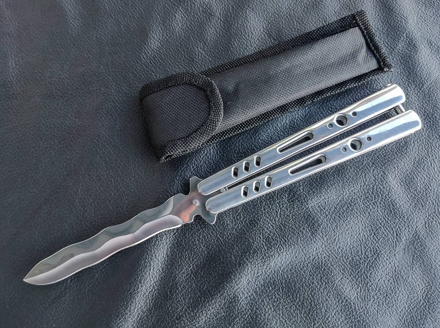 มีดบาลีซอง TK Tech มีดบาลิซองสไตล์เอเชีย ใบมีดเป็นทรงกริชสีเงิน ด้ามจับเป็นสแตนเลสฉลุลายสีเงินวาววับ จุดเด่นอยู่ที่ท้ายด้ามจับมีระบบสปริงแร็พ ทำให้หมุดล็อคด้ามไม่แกว่งไปมาในขณะเล่น จึงทำให้มิติของการควงสมดุล มาพร้อมซองไนล่อน