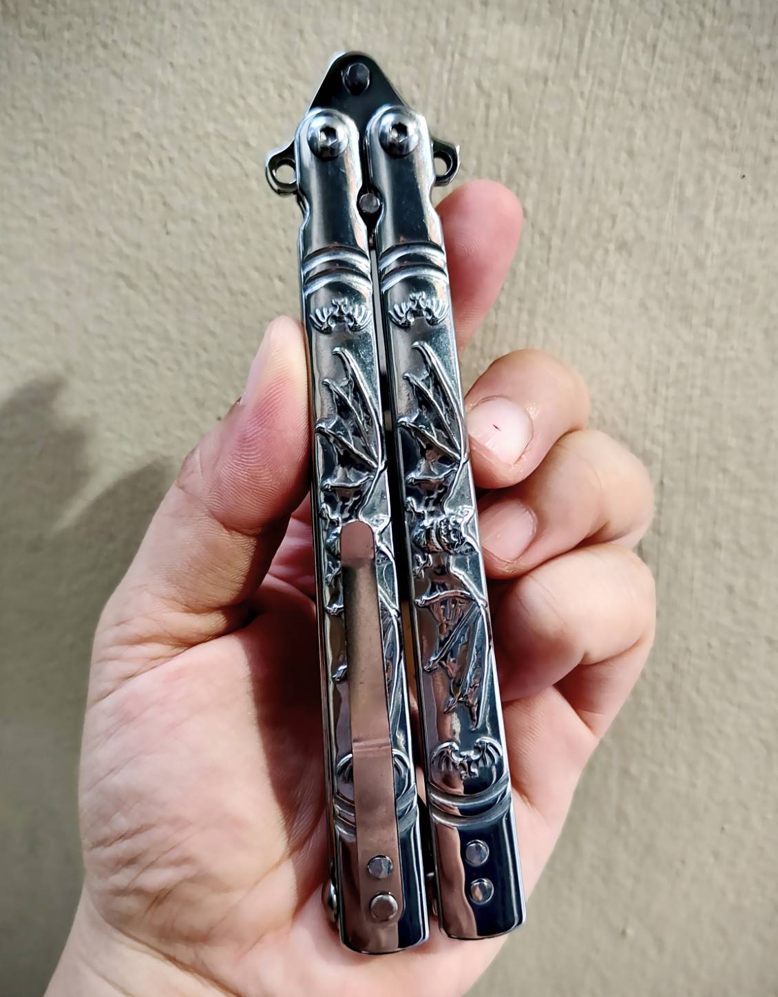 🦇 มีดควงค้างคาว เป็นบาลิซองสแตนเลส ขัดเงาเต็มตัว ใบทรงทันโตะ ปลายเฉียบ เส้นคมคมชัด ดูมีพลัง ด้ามแกะลายค้างคาวกางปีก รายละเอียดสวย งานนูนคมจนสัมผัสได้ ทั้งใบและด้ามเป็นสแตนเลส แข็งแรง จับแล้วรู้สึกถึงน้ำหนักพอดีมือ สายสะสม / สายชอบงานเงา / สายเท่เร