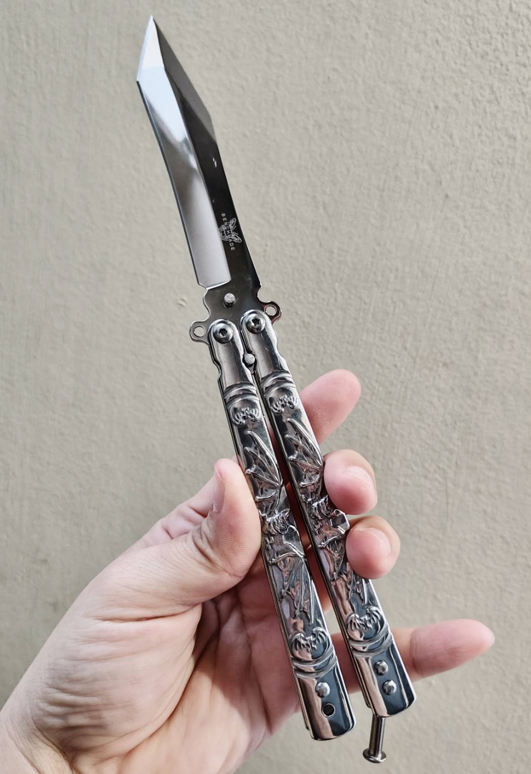 🦇 มีดควงค้างคาว เป็นบาลิซองสแตนเลส ขัดเงาเต็มตัว ใบทรงทันโตะ ปลายเฉียบ เส้นคมคมชัด ดูมีพลัง ด้ามแกะลายค้างคาวกางปีก รายละเอียดสวย งานนูนคมจนสัมผัสได้ ทั้งใบและด้ามเป็นสแตนเลส แข็งแรง จับแล้วรู้สึกถึงน้ำหนักพอดีมือ สายสะสม / สายชอบงานเงา / สายเท่เร