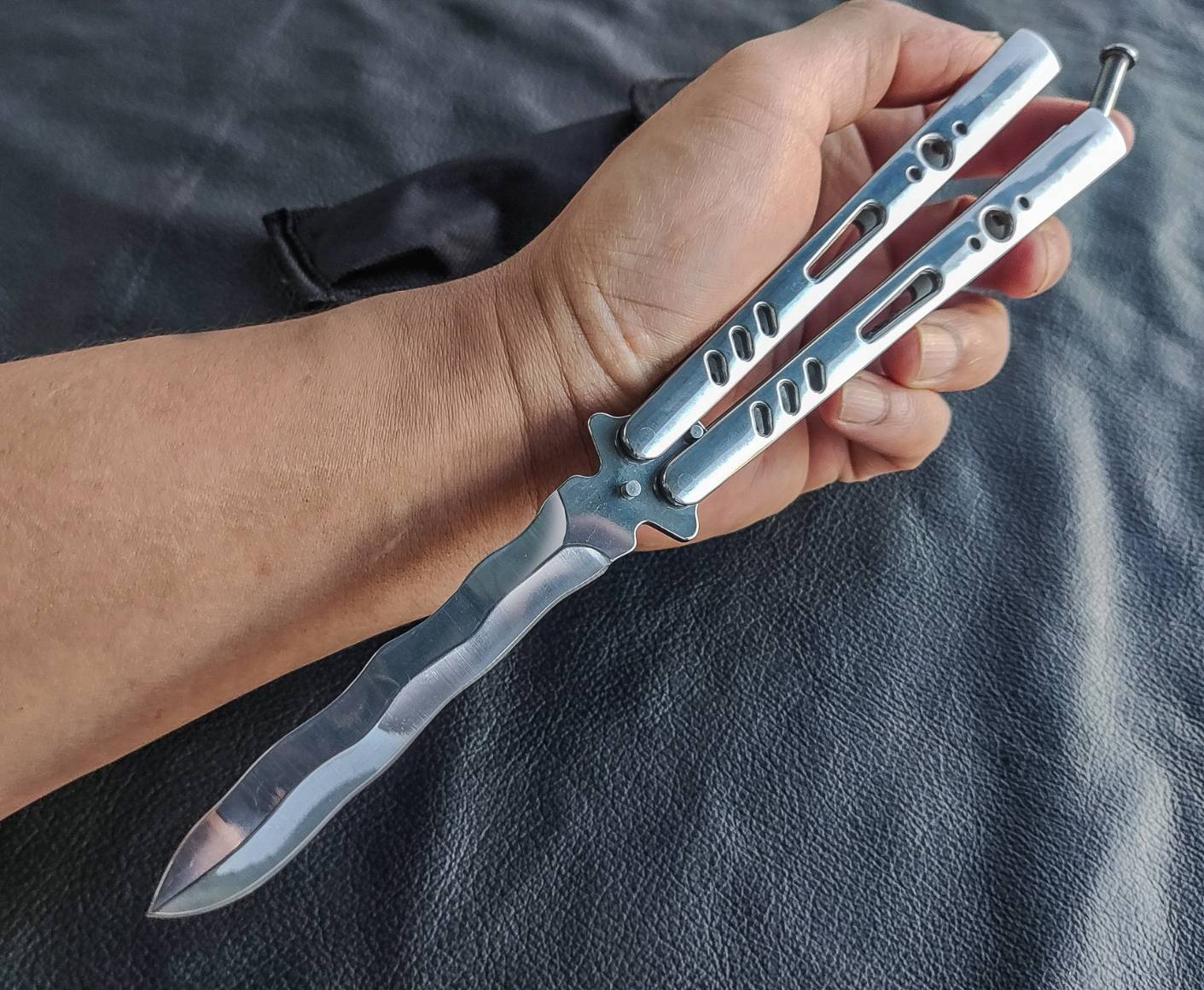 มีดบาลีซอง TK Tech มีดบาลิซองสไตล์เอเชีย ใบมีดเป็นทรงกริชสีเงิน ด้ามจับเป็นสแตนเลสฉลุลายสีเงินวาววับ จุดเด่นอยู่ที่ท้ายด้ามจับมีระบบสปริงแร็พ ทำให้หมุดล็อคด้ามไม่แกว่งไปมาในขณะเล่น จึงทำให้มิติของการควงสมดุล มาพร้อมซองไนล่อน